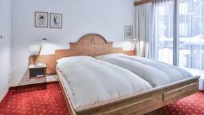 A hotel room with a wooden bed, a red patterned carpet, and two framed pictures on the wall. - Chalet Abendrot apARTments by Interhome (Grindelwald)
