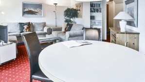 A modern living room with a round dining table, grey sofas, a bookshelf, and a wooden ceiling. - Chalet Abendrot apARTments by Interhome (Grindelwald)