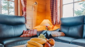 Een gezellige kamer met houten inrichting, twee leren banken, een houten tafel met een schaal fruit, en een lamp.