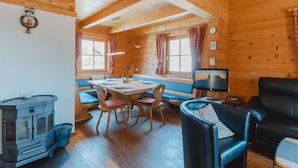 Een gezellig interieur van een chalet met een eethoek, een bank, een televisie en een houtkachel.