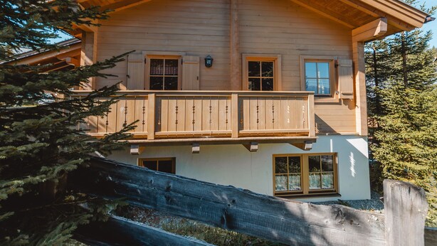 Een houten huis met twee verdiepingen, een balkon, grote ramen en een schuin dak.
