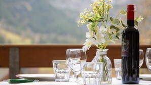Una mesa dispuesta para comer, con una botella de vino tinto, un florero de vidrio con flores blancas y vasos para beber.