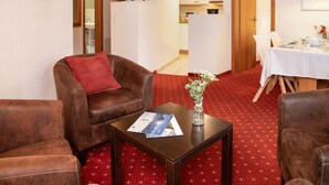 Una sala de estar con un sofá de cuero marrón, una mesita de madera con una revista y un florero con flores, y una alfombra roja con estampado.