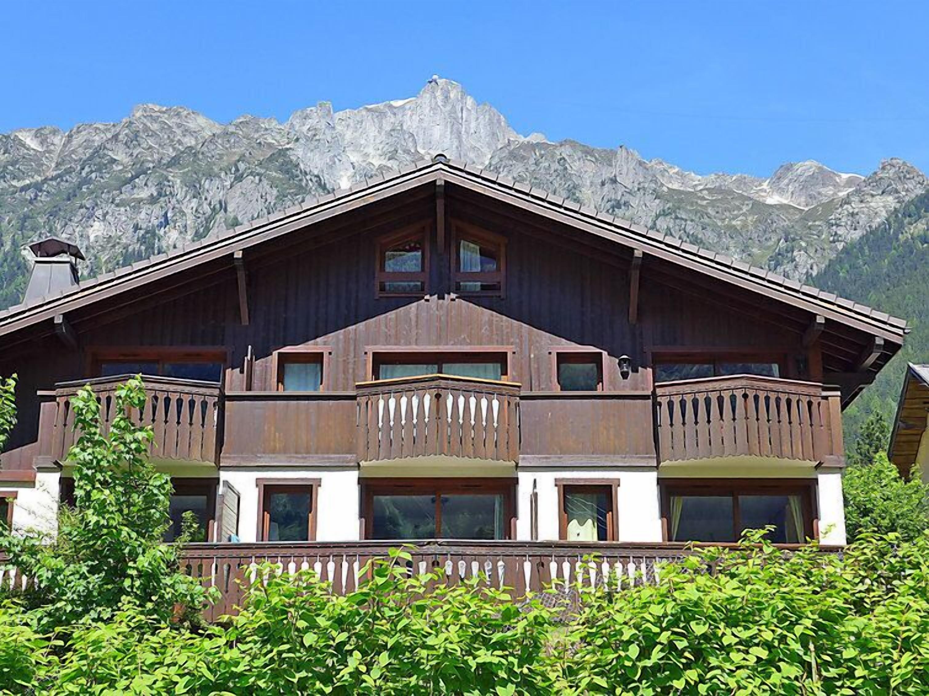 A chalet with a wooden facade, multiple balconies, and a mountainous backdrop.