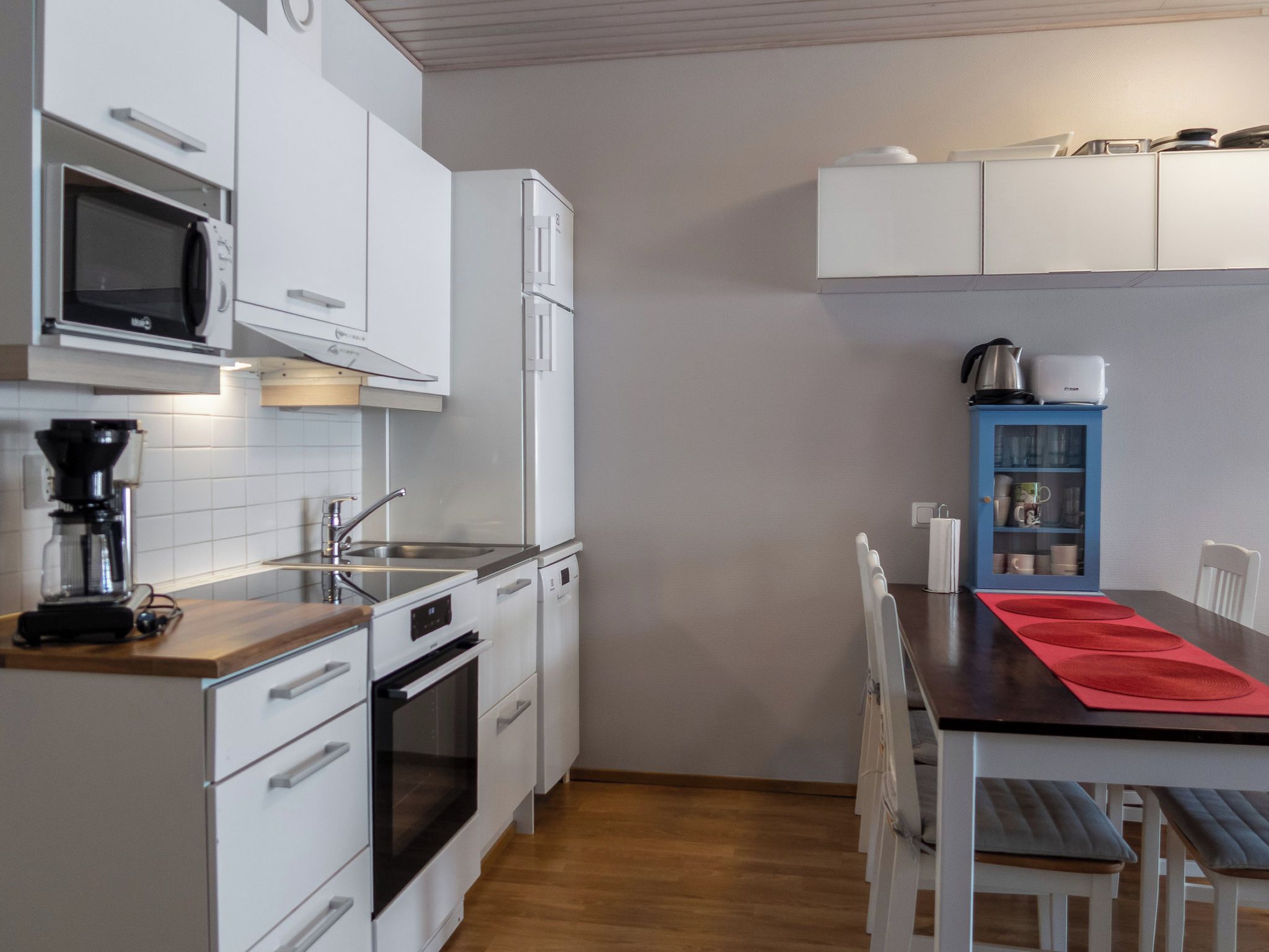 A modern kitchen with white cabinetry, a built-in oven, a coffee maker, and a blue cabinet with dishes.