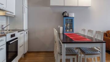 Una cocina compacta con armarios blancos, estufa y una zona de comedor con un mantel individual rojo.
