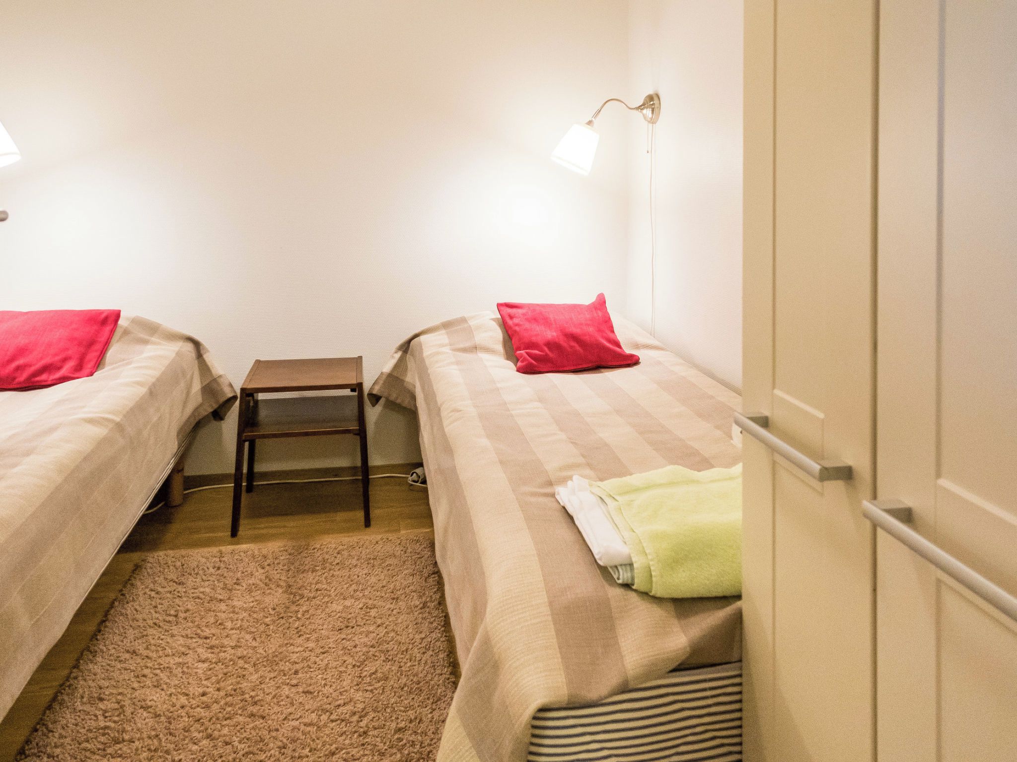A small, clean room with two beds, a small table, and a lamp.