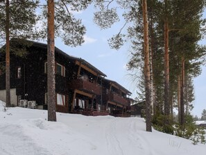 A wooden cabin with a porch, surrounded by tall pine trees and covered in snow. - Vacation home Kerttu by Interhome (Sotkamo)