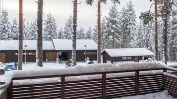 A snow-covered landscape with a wooden fence, a building with a snow-covered roof, and tall pine trees.