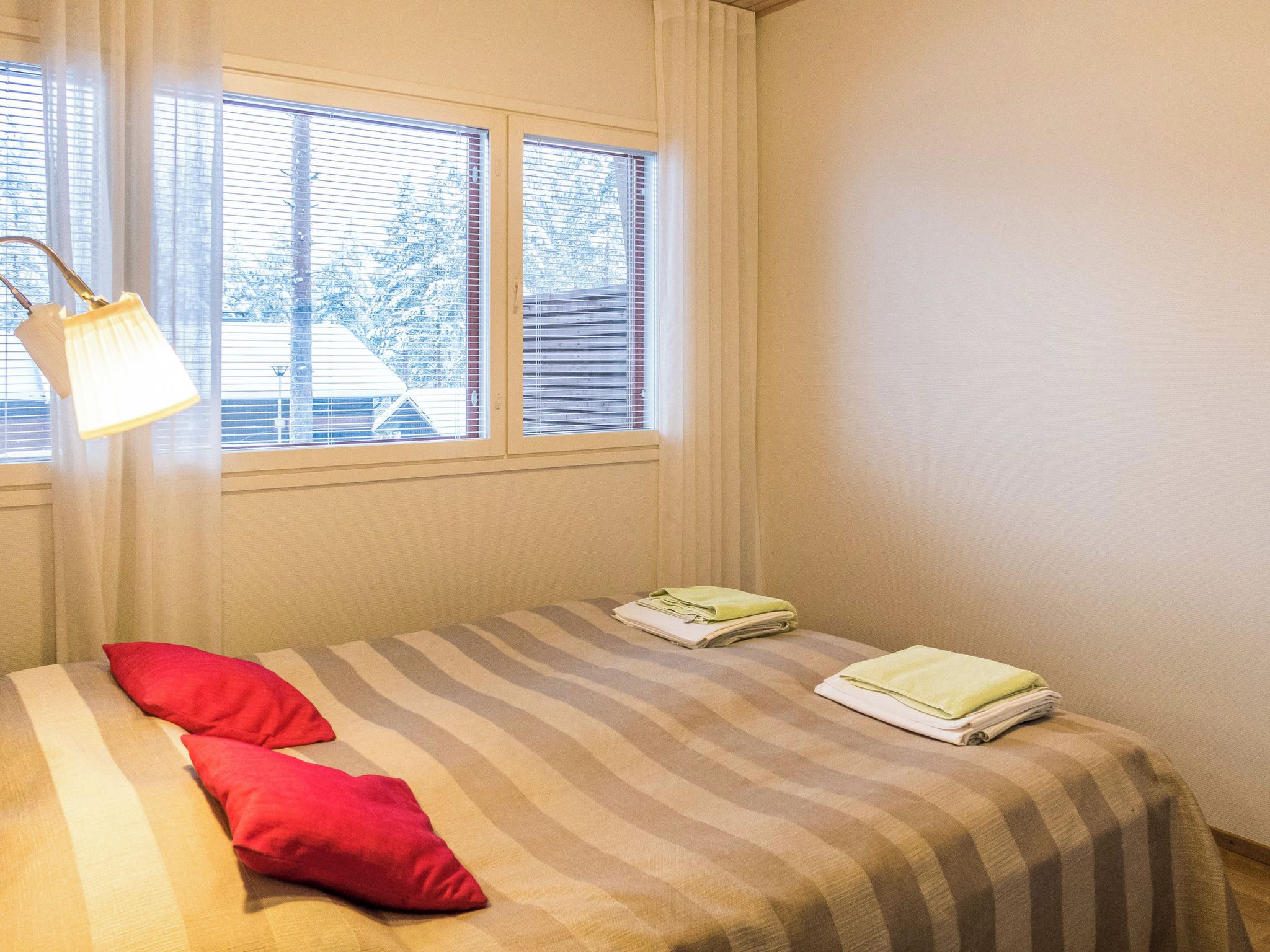 A bedroom with a bed, two pillows, a window with blinds, and a lamp.