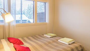 A bedroom with a bed, two pillows, a window with blinds, and a lamp.