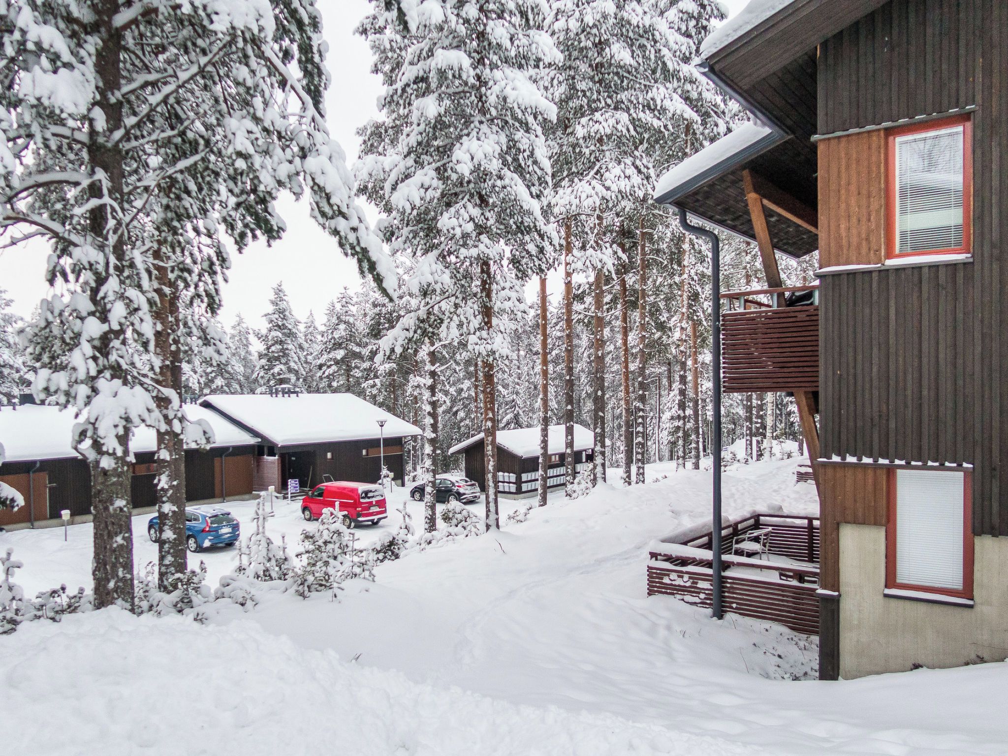 A snow-covered lodge with multiple cabins, a parking area with vehicles, and a wooden deck.