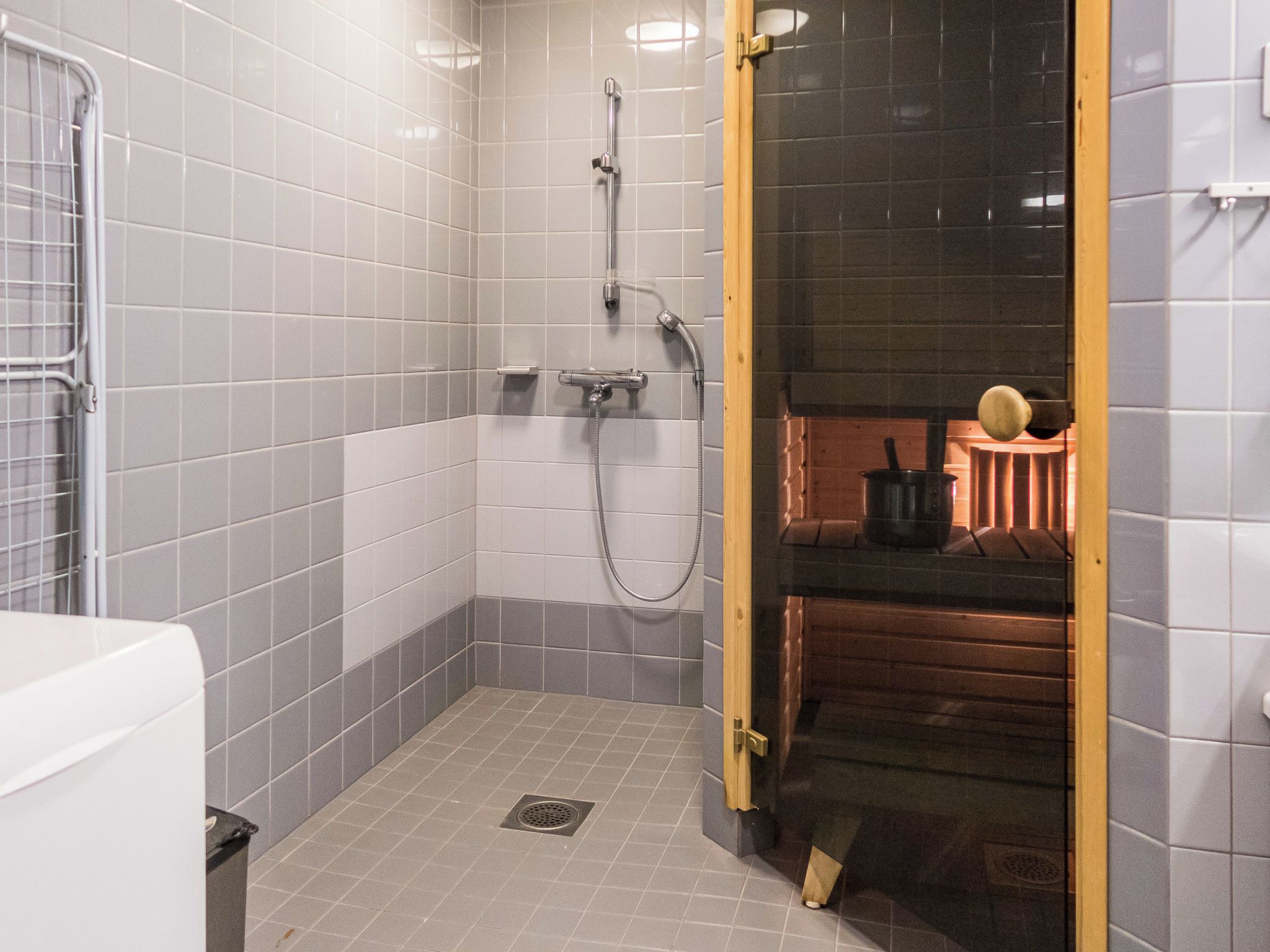 A small, tiled bathroom with a shower, a toilet, and a wooden door leading to a different room.