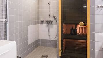 A small, tiled bathroom with a shower, a toilet, and a wooden door leading to a different room.