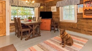 A cozy cabin interior with a dining area, a television, and a dog sitting on a rug.