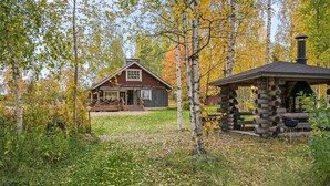 A rustic cabin with a wooden deck and a stone structure in a forested area.