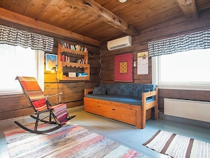 A cozy cabin interior with a rocking chair, a sofa, a bookshelf, and a window with curtains.