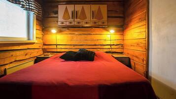 Ein Zimmer einer Holzhütte mit einem Bett, zwei Nachttischen und einem Fenster mit Vorhängen.