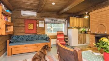 Ein gemütliches Blockhaus-Interieur mit Holzbalkendecke, einer Couch, einem Hund, einem Esstisch und einer Küchenzeile.