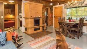 A cozy cabin interior with a fireplace, wooden walls, a dining area, and a dog.