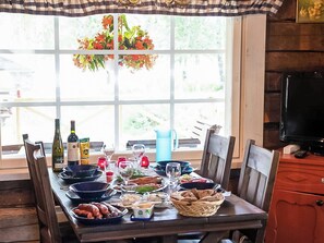 A dining table set with various dishes, glasses, and bottles, positioned in front of a large window with a view of greenery.