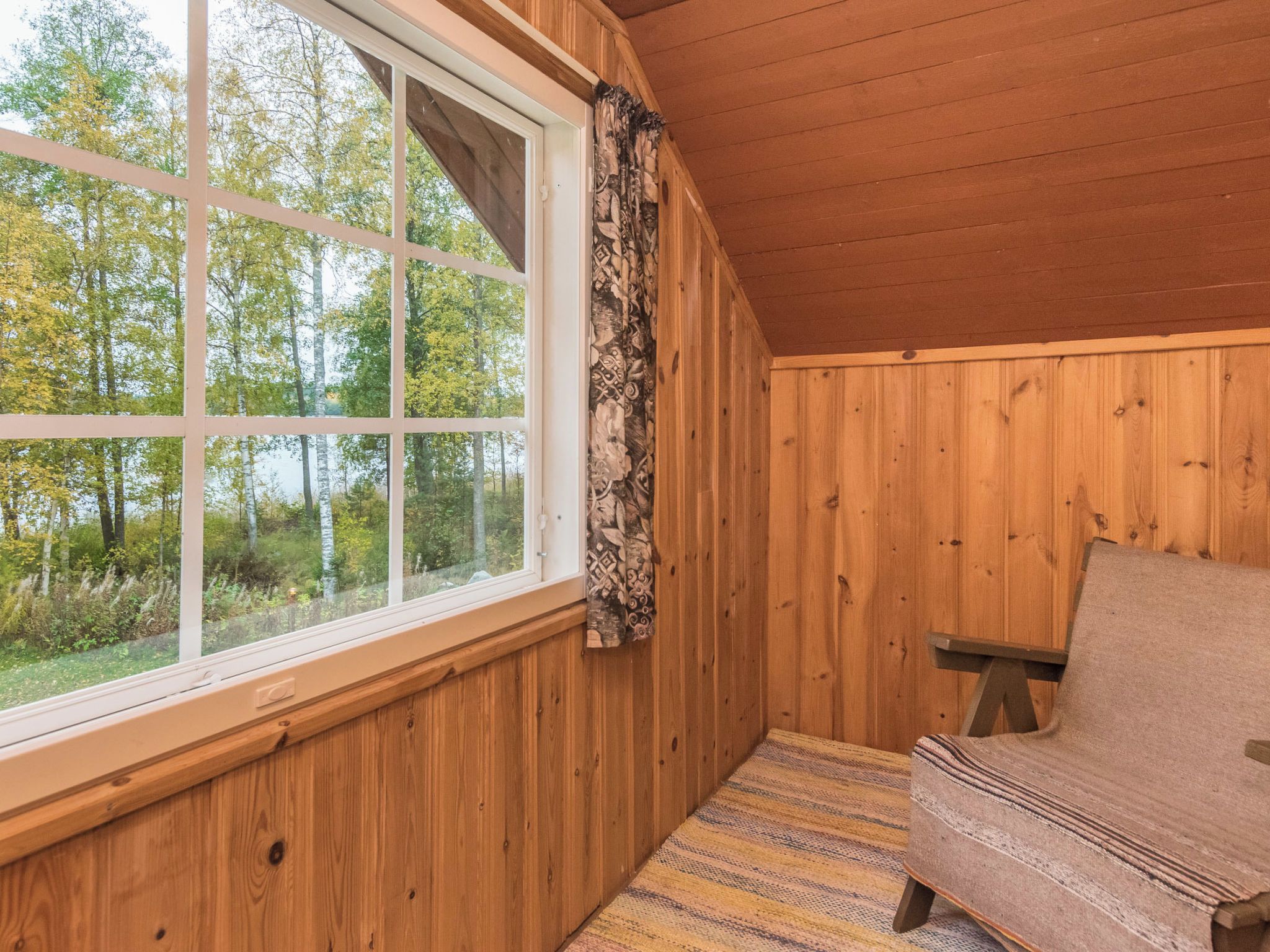 A cabin with a large window, wooden walls, and a chair.