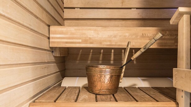 Een sauna met houten banken en een koperen emmer met een schaal.