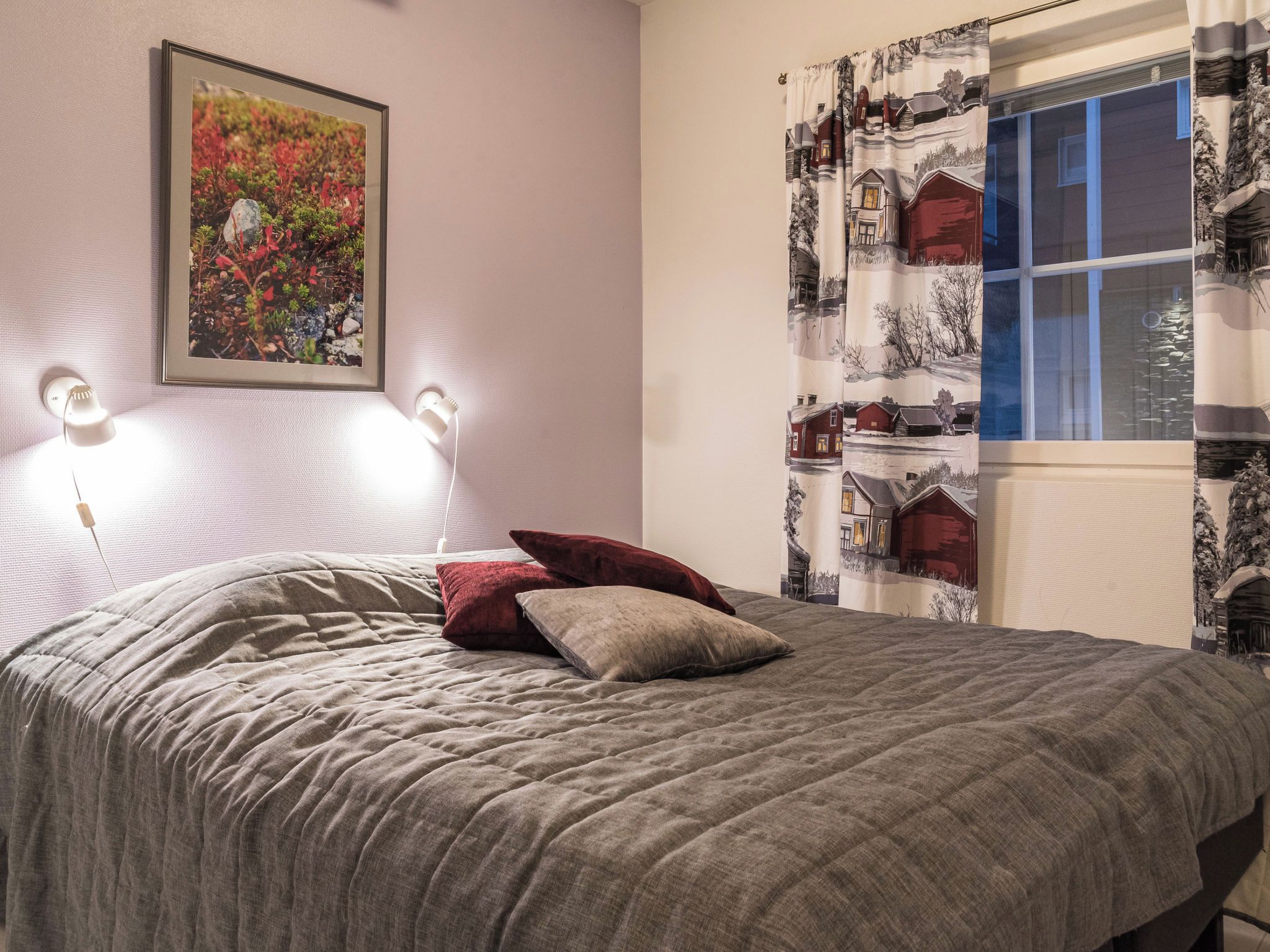 A bedroom with a bed, a framed picture on the wall, and a window with curtains.