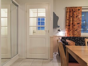 Ein Zimmer mit einer weißen Tür, einem Fenster mit Jalousien, einem gemusterten Sofa und einem Holztisch.