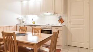 Een kleine keuken met witte kastjes, een fornuis en een eettafel met stoelen.