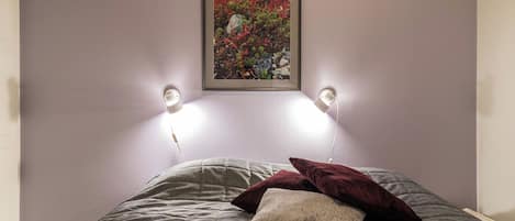 Ein Bett mit einer grauen Tagesdecke, zwei Kissen und einem darüber hängenden Bild.