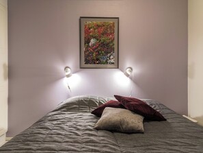 Ein Bett mit einer grauen Tagesdecke, zwei Kissen und einem darüber hängenden Bild.