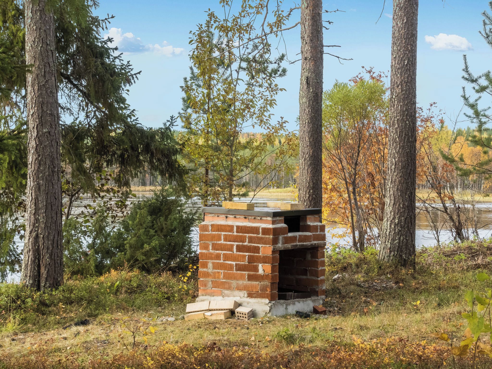A brick-built outdoor structure, possibly a barbecue or grill, surrounded by trees and a body of water.