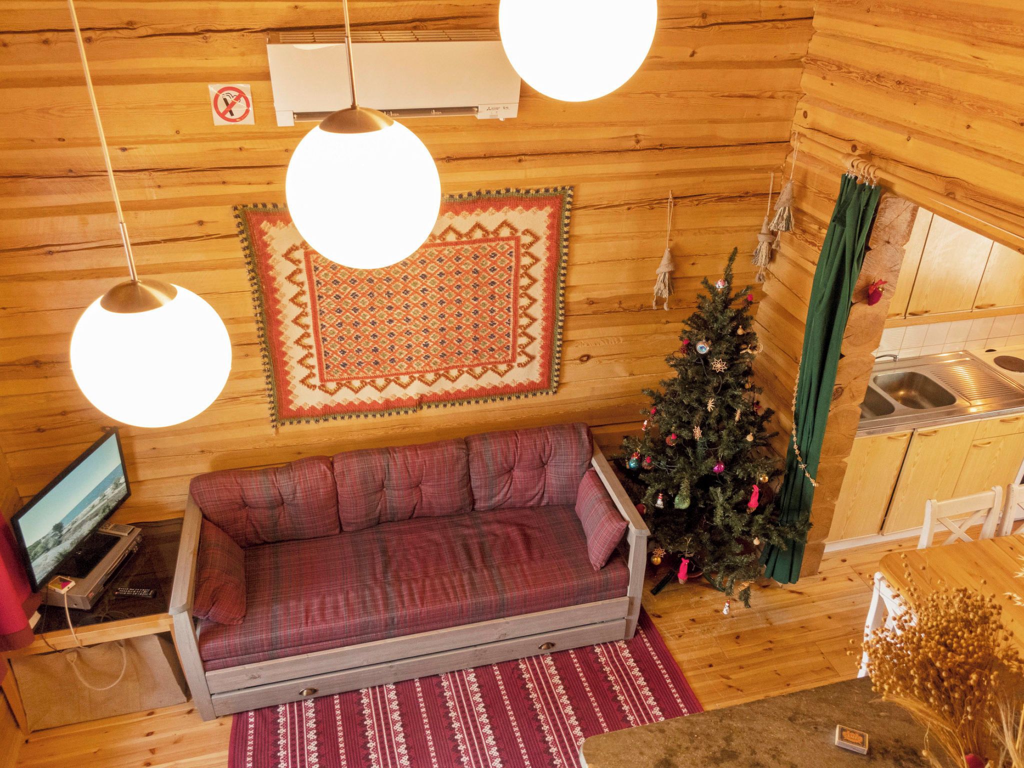 Un interior acogedor de cabaña con sofá, televisor, árbol de Navidad y área de cocina.