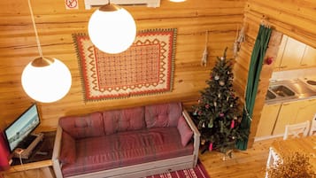 Un interior acogedor de cabaña con sofá, televisor, árbol de Navidad y área de cocina.