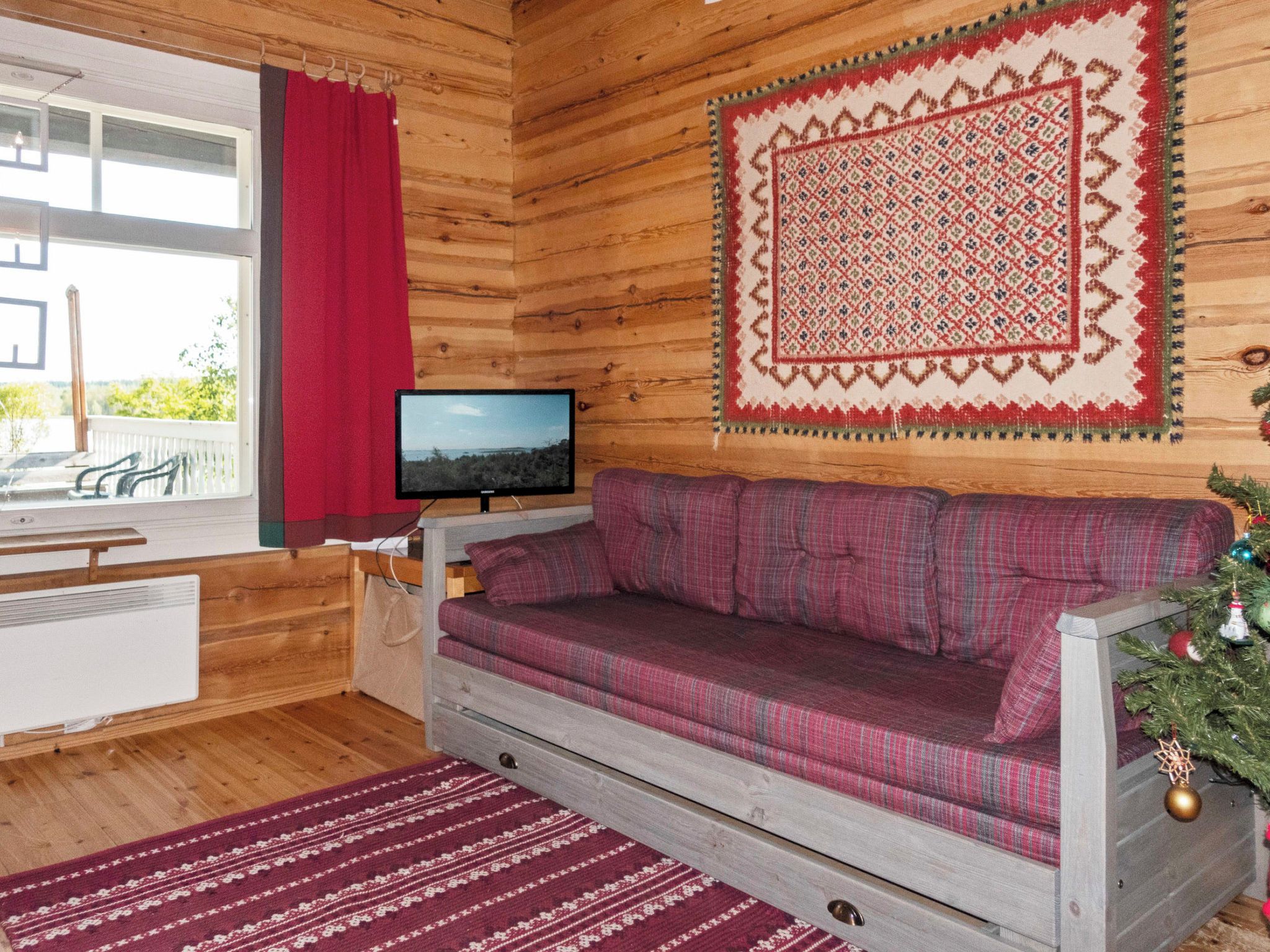 A cozy cabin interior with a wooden interior, a television on a small table, a plaid sofa, and a decorative rug.