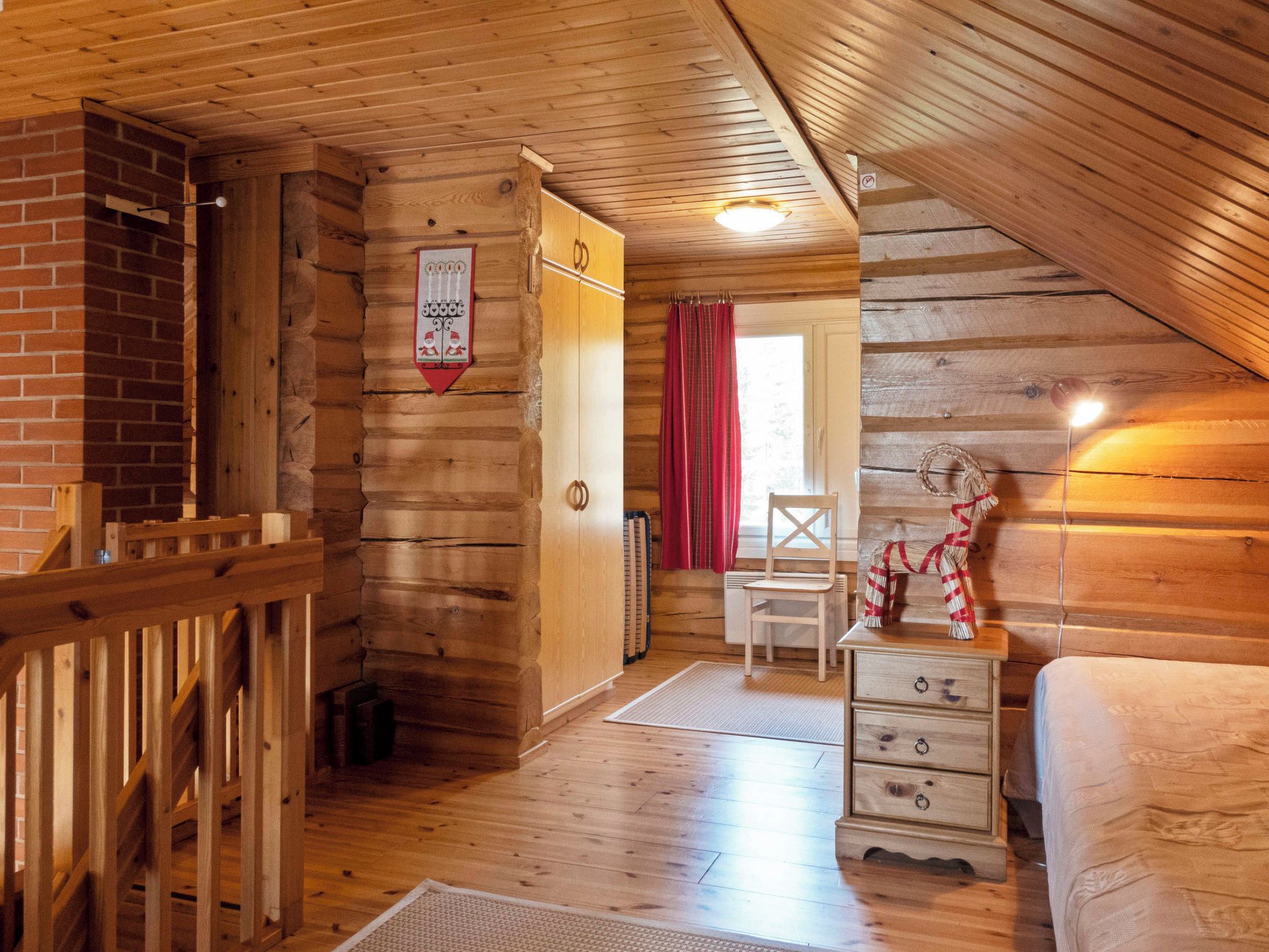 Interior de una cabaña de troncos con escaleras de madera, una cama, un aparador y una silla.