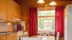 A cozy kitchen with wooden cabinets, a dining table with chairs, a refrigerator, and a window with curtains.