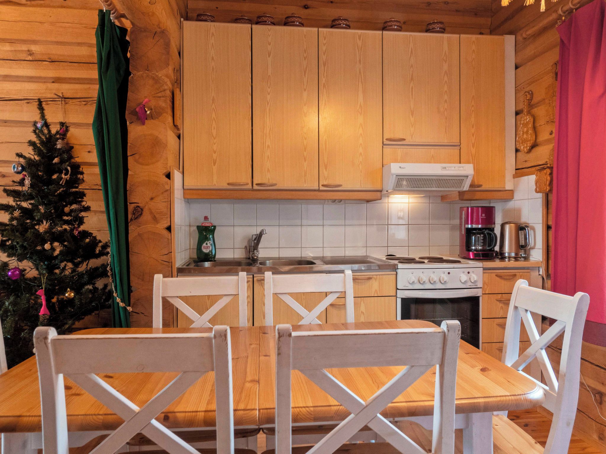 A wooden cabin kitchen with a dining table and chairs, a stove, and a coffee maker.