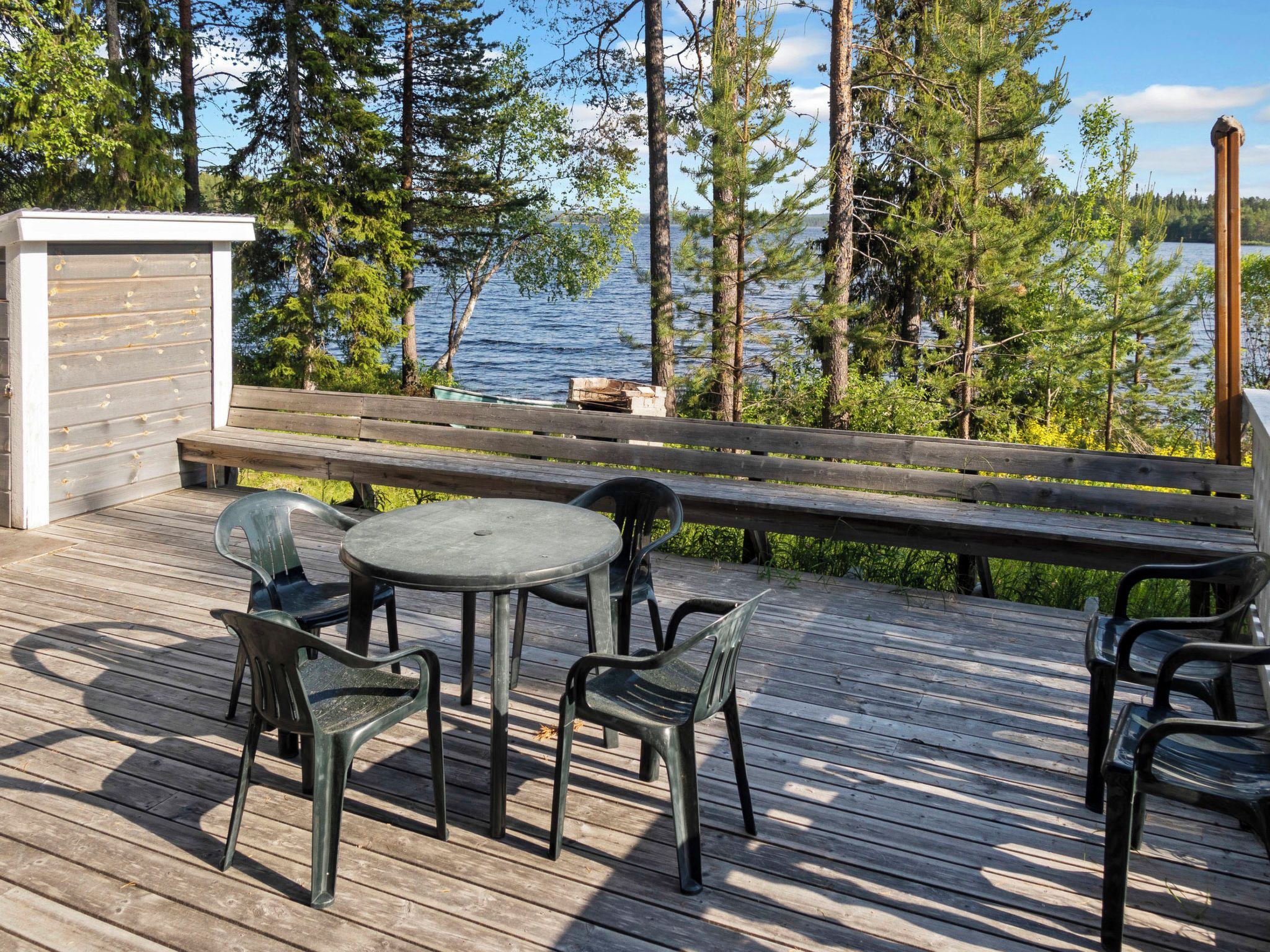 A wooden deck with a round table and chairs, overlooking a lake with trees.