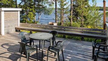 A wooden deck with a round table and chairs, overlooking a lake with trees.