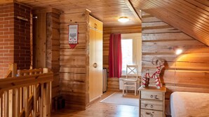 A cozy log cabin room with wooden walls and floors, a wooden staircase, a bed, a dresser, and a chair.