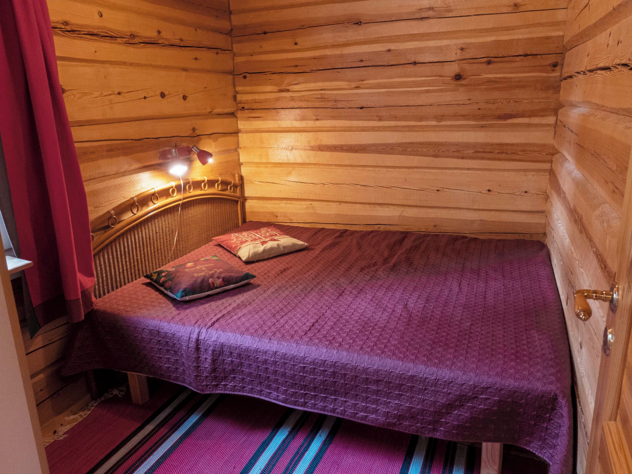 A wooden cabin room with a bed, a headboard, and a window with curtains.