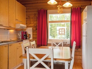 Puinen mökki, jonka sisätiloissa on keittiö, ruokapöytä, tuoleja ja jääkaappi.