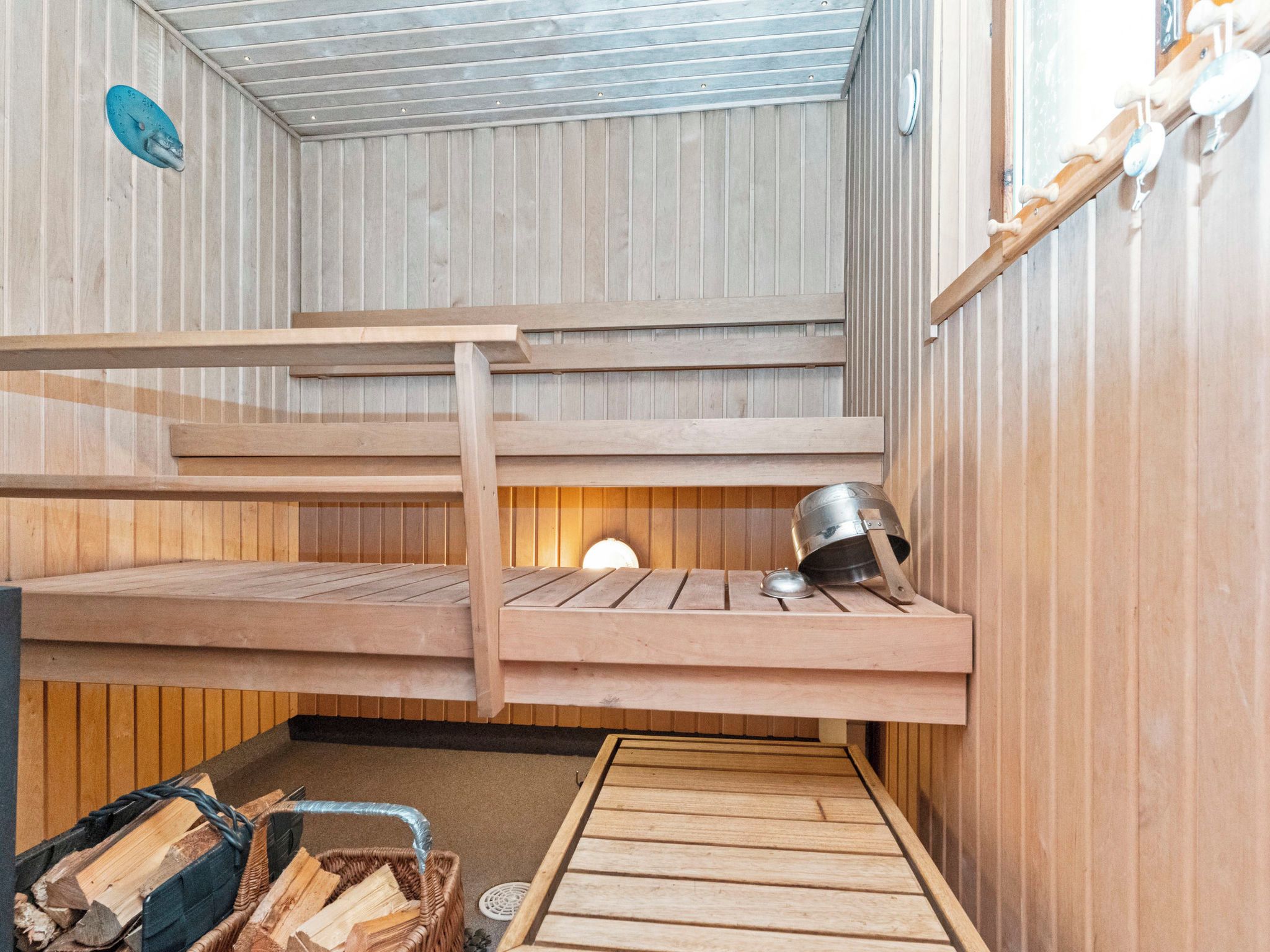 A sauna with wooden benches, a metal bucket, and a log storage area.