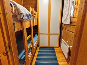 Un pasillo estrecho con paredes de madera, una cama litera, un pequeño armario blanco y un tapete azul a rayas.
