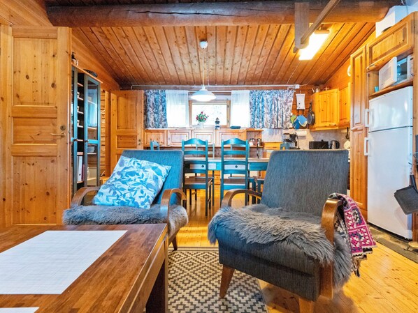 Ein gemütliches Blockhaus-Interieur mit Holzwänden, einem Essbereich mit Stühlen und Tisch sowie einer Küche mit Schränken und Geräten.