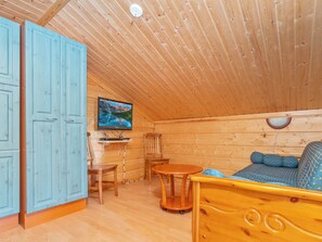 Ein gemütliches Blockhaus-Interieur mit Holzbalkendecke, einem Bett mit blauer Bettwäsche, einem Fernseher an der Wand und einem Holztisch.