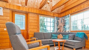 Un acogedor interior de cabaña con un sofá gris, una silla de madera y una mesita.