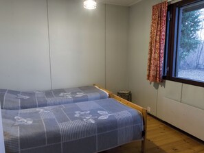 Een kamer met twee bedden, een klein tafeltje en een raam met gordijnen.